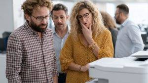 Office Frustration: A team grapples with the complexities of a printer in a modern office setting, portraying the common challenges of office life and technical difficulties