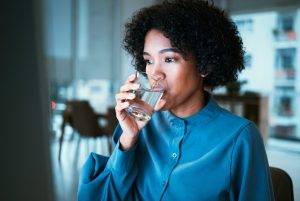 Woman, drinking water and night in office, reading or thinking for hydration, wellness or finance company. Accountant, glass and computer for nutrition, diet or detox for health, idea or workplace. 