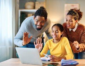 Mother, father and daughter meeting with teacher online with laptop at home using VoIP. 